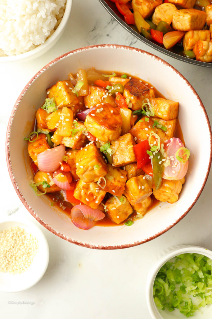 sweet and sour tempeh with pineapple in a bowl sprinkled with sesame seeds and chopped spring onions
