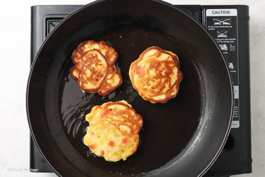 three corn fritters fried in a pan over a medium heat