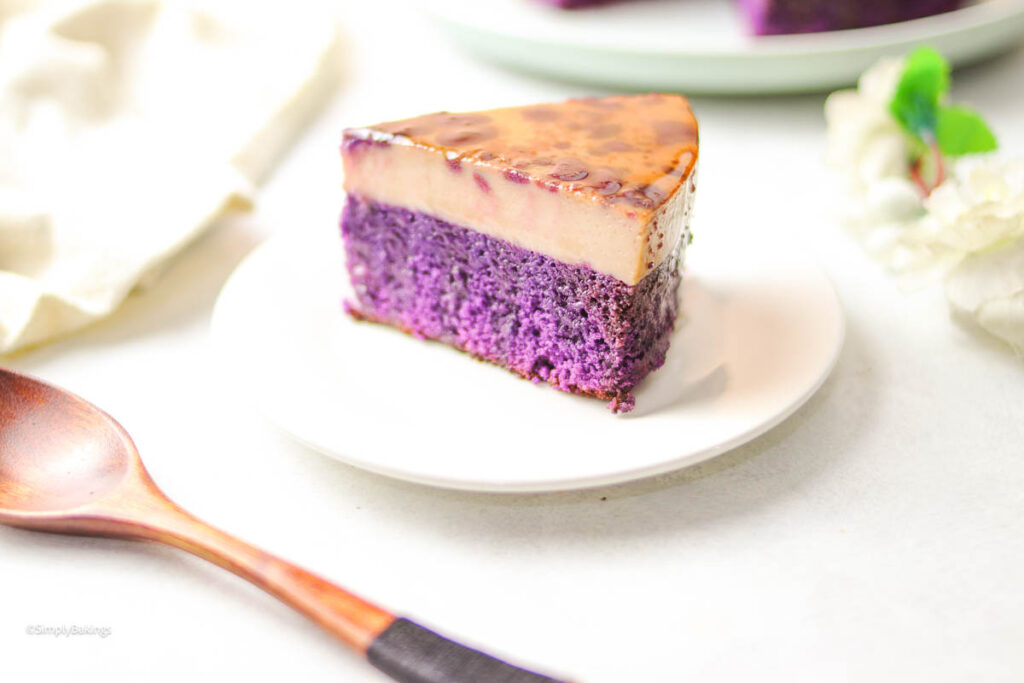 a slice of Ube Flan on a white plate next to a wooden spoon on a white surface