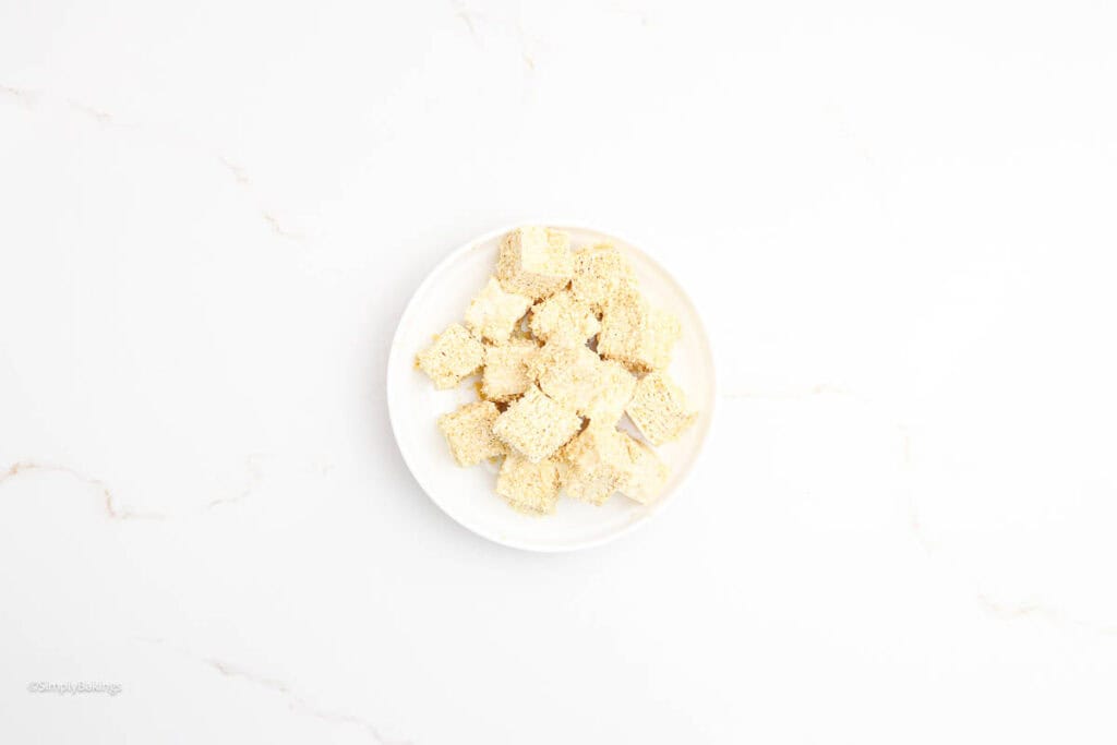 A white plate of some coated tofu cubes