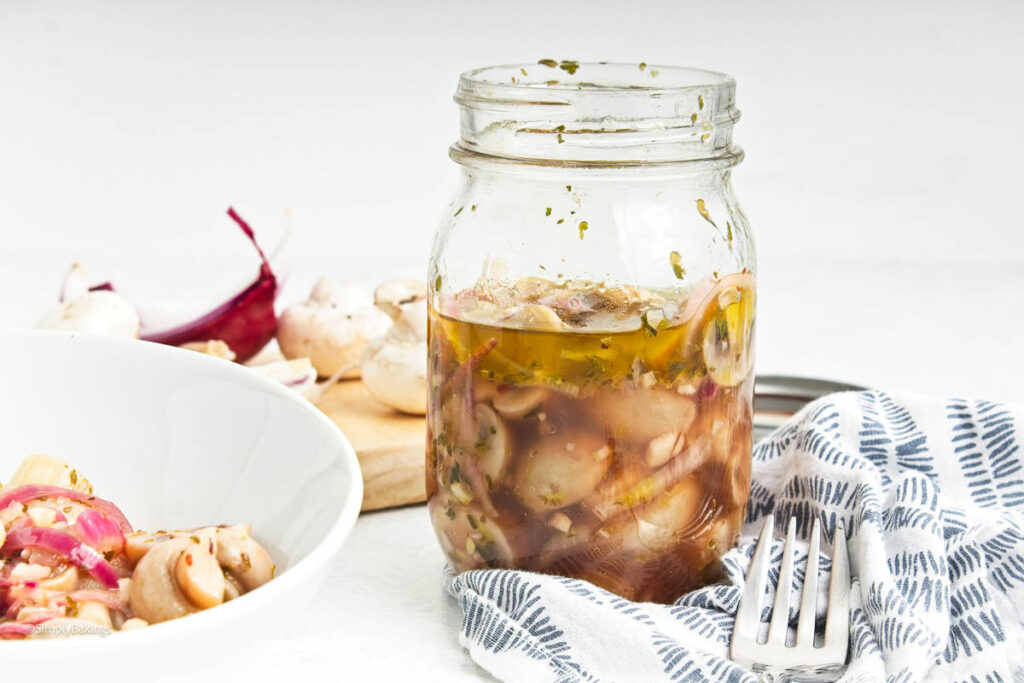 A jar of Soy Marinated Mushrooms next to a white bowl with some soy marinated mushrooms