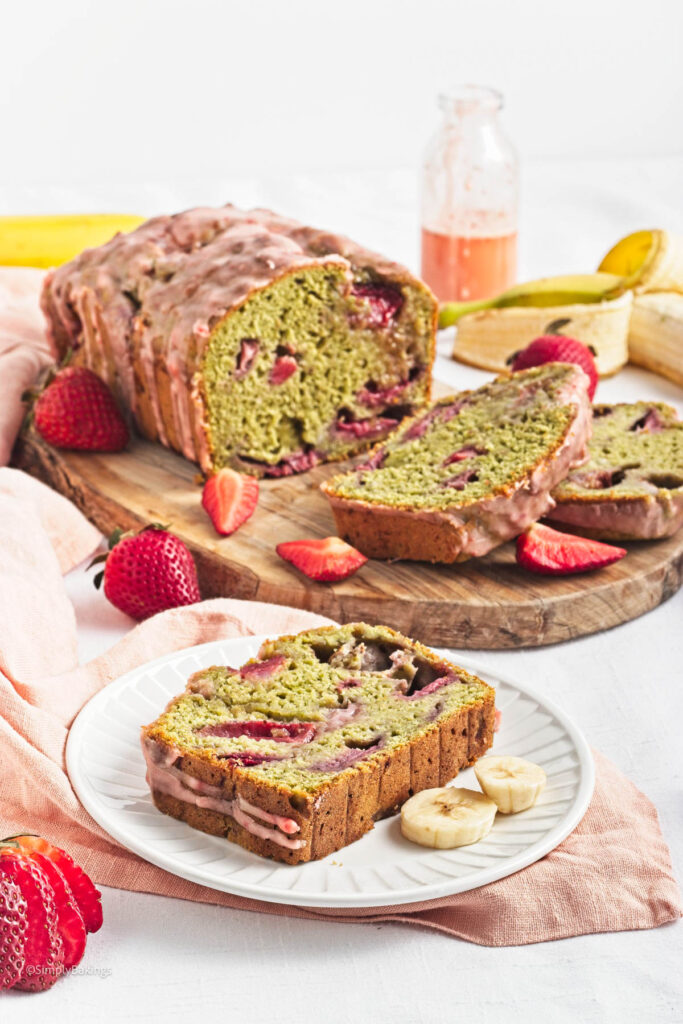 A sliced loaf of Strawberry Matcha Bread on a wooden board garnished with strawberry slices and a slice of it served on a white plate