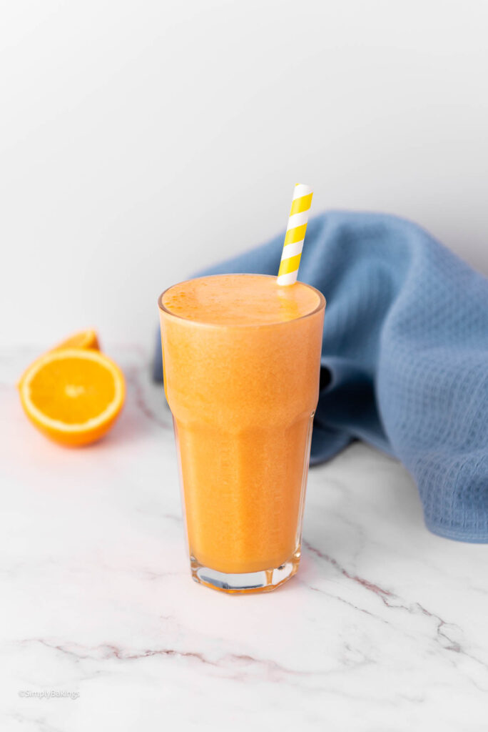 Ginger Orange Juice in a tall glass with slices of orange and a blue cloth in the background