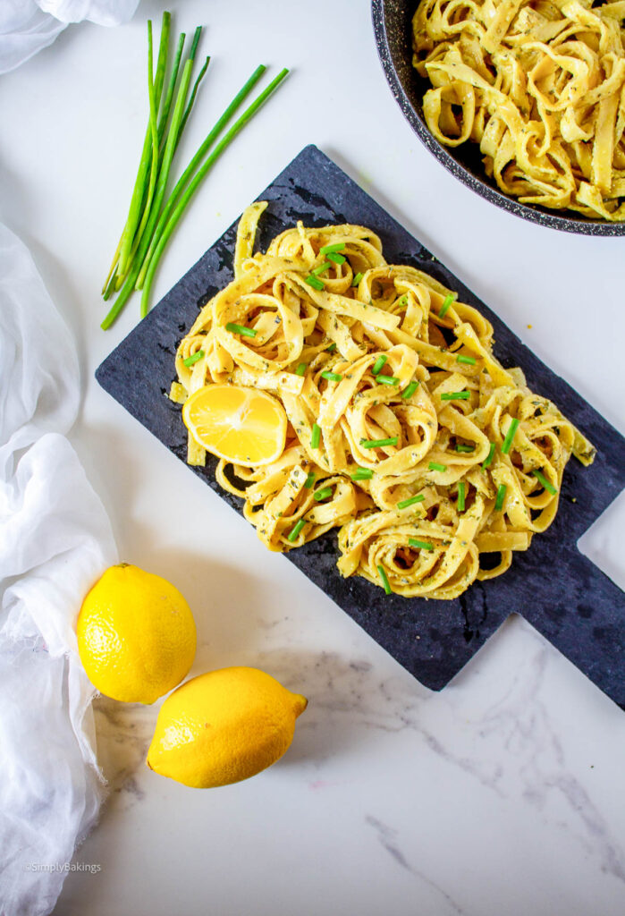 Vegan Lemon Pasta on a wooden board garnished with a slice of lemon and green onion slices