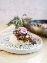 Eggplant bisteak in a white bowl topped with white onion slices