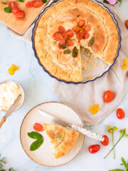 freshly baked Focaccia with Tomatoes and Onions on a circular pan and a slice of it on a small white plate with a knife
