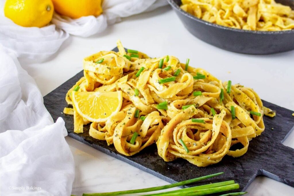 Vegan lemon pasta on a wooden table garnished with green onion slices