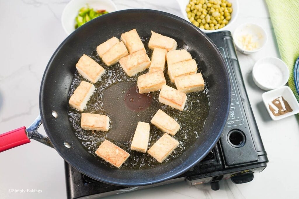 Tofu cubes frying in a black pan