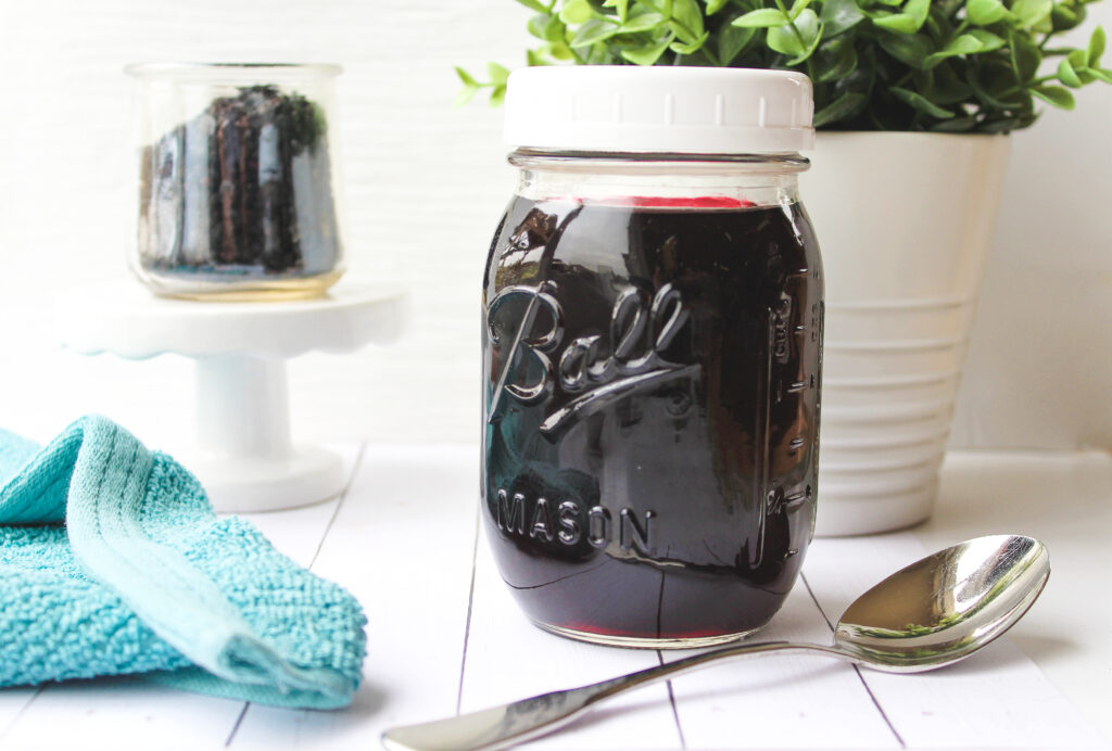 elderberry syrup inside a glass jar and a spoon beside it. 