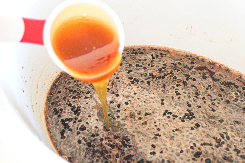 pouring honey in a bowl of elderberry juice